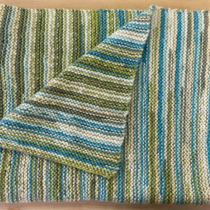 Close-up of a striped knitted blanket in shades of green, blue, and cream, demonstrating the finished product of the "You & Me Blanket Pattern"