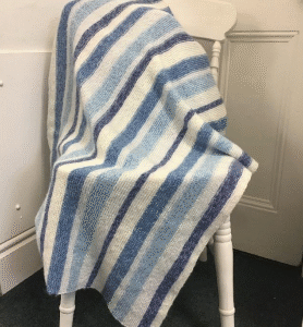 Striped knitted blanket in shades of blue, white, and gray, draped over a white wooden spindle chair.